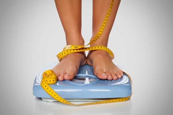 Woman Standing on Bathroom Scales With a Measuring Tape Wrapped Around Her Feet